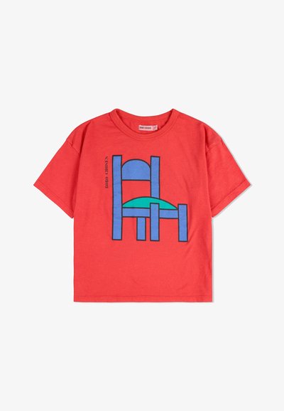 T-shirt di cotone rosso con un design grafico di una sedia blu con seduta turchese. La maglietta ha maniche corte e collo rotondo.