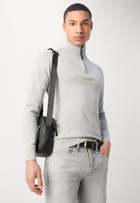 Pull léger gris clair à fermeture éclair en tricot doux, associ�é à un jean gris clair et à un sac bandoulière noir. Une ceinture noire avec une boucle dorée accentue la tenue.