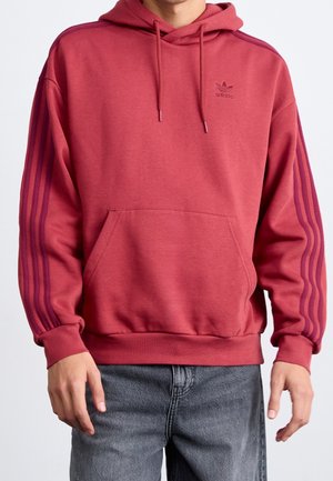Röd bomullshuvtröja med framficka, dragsko i huvan och tre lila ränder på varje ärm. Adidas-logotyp på bröstet.