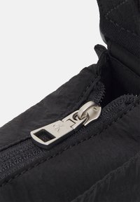 Černá zavírací taška s texturovanou tkaninou, vybavená robustním kovovým zipem a diskrétním štítkem značky. Kompaktní, funkční design pro všestranné použití.