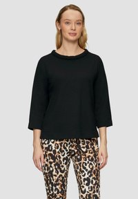Zwart driekwart mouwtop met een ronde halslijn, van een gestructureerde stof, gecombineerd met een broek met een panterprint.