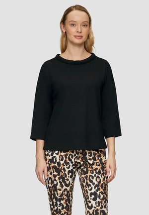 Haut noir à manches trois-quarts avec un col rond, en tissu texturé, associé à un pantalon à motifs léopard.