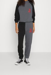 Grå och svart matchande träningsdräkt med röd logotyp; sweatshirten har raglanärmar, och byxorna har färgblockering och avsmalnande muddar. Svarta sneakers.