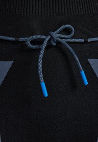 Zwarte stof met een gemêleerd breisel, voorzien van een trekkoordsluiting gemaakt van blauw gevlochten touw met kunststof uiteinden. Geometrisch patroon in grijs.