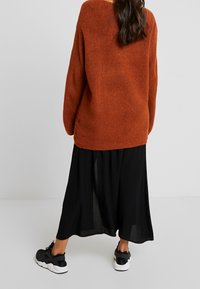 Rostfärgad stickad tröja, oversized passform, med långa ärmar. I kombination med en svart flödande kjol och svarta sportskor.