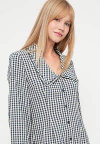 Μπλούζα νάυ και κρέμα με καρό σχέδιο, με κολάρο, διαθέτει κουμπάκια μπροστά και μακριά μανίκια. Υφασμάτινη υφή με άνετη εφαρμογή.