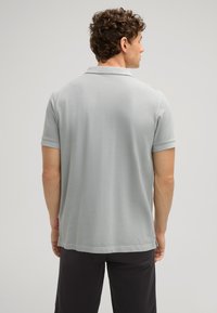 Lichtgrijze polo met korte mouwen, een platte kraag en een label aan de zoom. Zachte textuur en casual ontwerp.