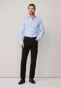 Lichtblauw overhemd met knopen, donkere slim-fit broek en zwarte leren schoenen. Heeft lange mouwen met knoopmanchetten en subtiele logo-details.