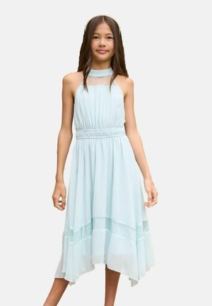 Tüdruk kannab varrukateta helesinist kaela taha seotud kleiti pitsilistest aktsentidest ja elastse vööosaga, seisab ühevärvilise tausta ees.