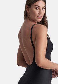 Bañador negro con tirantes finos y un diseño de espalda profunda. El material parece suave, sin patrones ni acentos visibles.