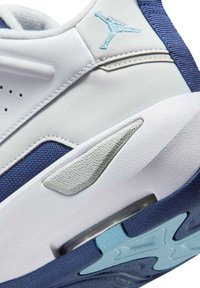 Baskets blanches et marines avec une tige en cuir lisse et en mesh, présentant un accent texturé gris et une semelle extérieure translucide bleue.