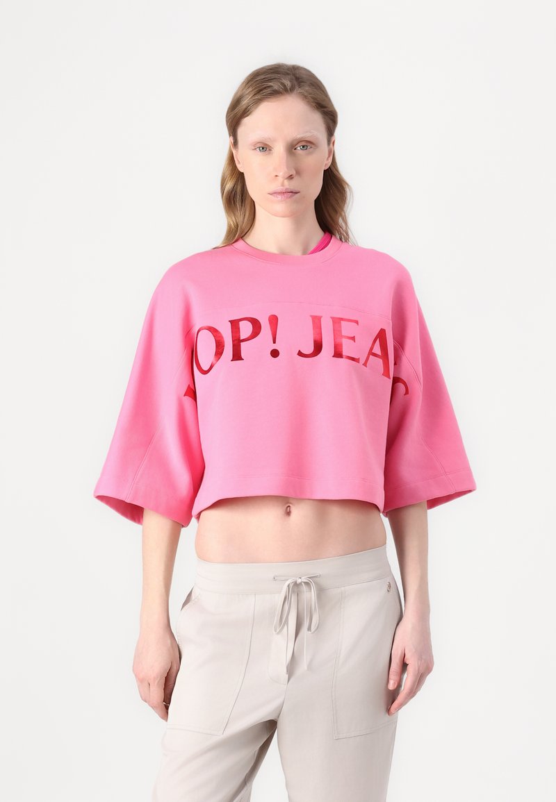 Pink cropped sweatshirt with a round neckline and short, wide sleeves. Features bold red text "OP! JEANS" across the chest.