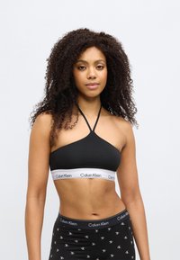 Μαύρο μπουστάκι halter με λευκή ταινία λογότυπου Calvin Klein. Λείο υλικό, απλός, εφαρμοστός σχεδιασμός. Μαύρο κολάν με διακοσμητικά λογότυπα.