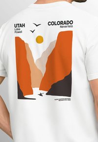 Weißes T-Shirt mit einem grafischen Design, das orange und beige Berge, eine Sonne und einen Kajakfahrer zeigt, betitelt mit "Utah Lake Powell" und "Colorado Neverless."