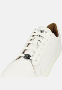 Sneaker in pelle bianca con texture liscia, punta rotonda e lacci piatti. Accento con logo nero sulla linguetta e dettagli di cucitura sottili.