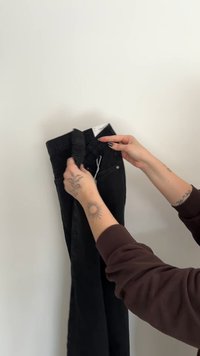 Czarne dżinsy z denimu trzymane w ręku, z wysokim stanem, pięcioma kieszeniami i widocznymi przeszyciami.