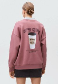 Verblasster rosa Sweatshirt mit lockerer Passform, versehen mit einem Grafikdruck einer Kaffeetasse und Text auf der Rückseite. Baumwollmischung mit gerippten Bündchen und Saum.