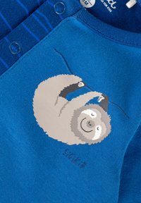 Camicia di cotone blu con una grafica di un bradipo in grigio e bianco, con bottoni e una texture a righe sulla spalla.