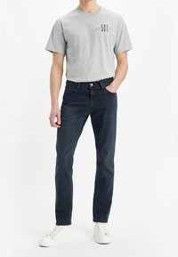 Grå bomulls-t-shirt med en "501" grafik i svart och rosa, kombinerad med mörka jeans och vita sneakers. Enkel, avslappnad outfit.