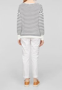 Maglione a righe bianco e blu navy, con vestibilità ampia, polsini a costine e scollatura rotonda, abbinato a jeans bianchi arrotolati e sneakers color beige.
