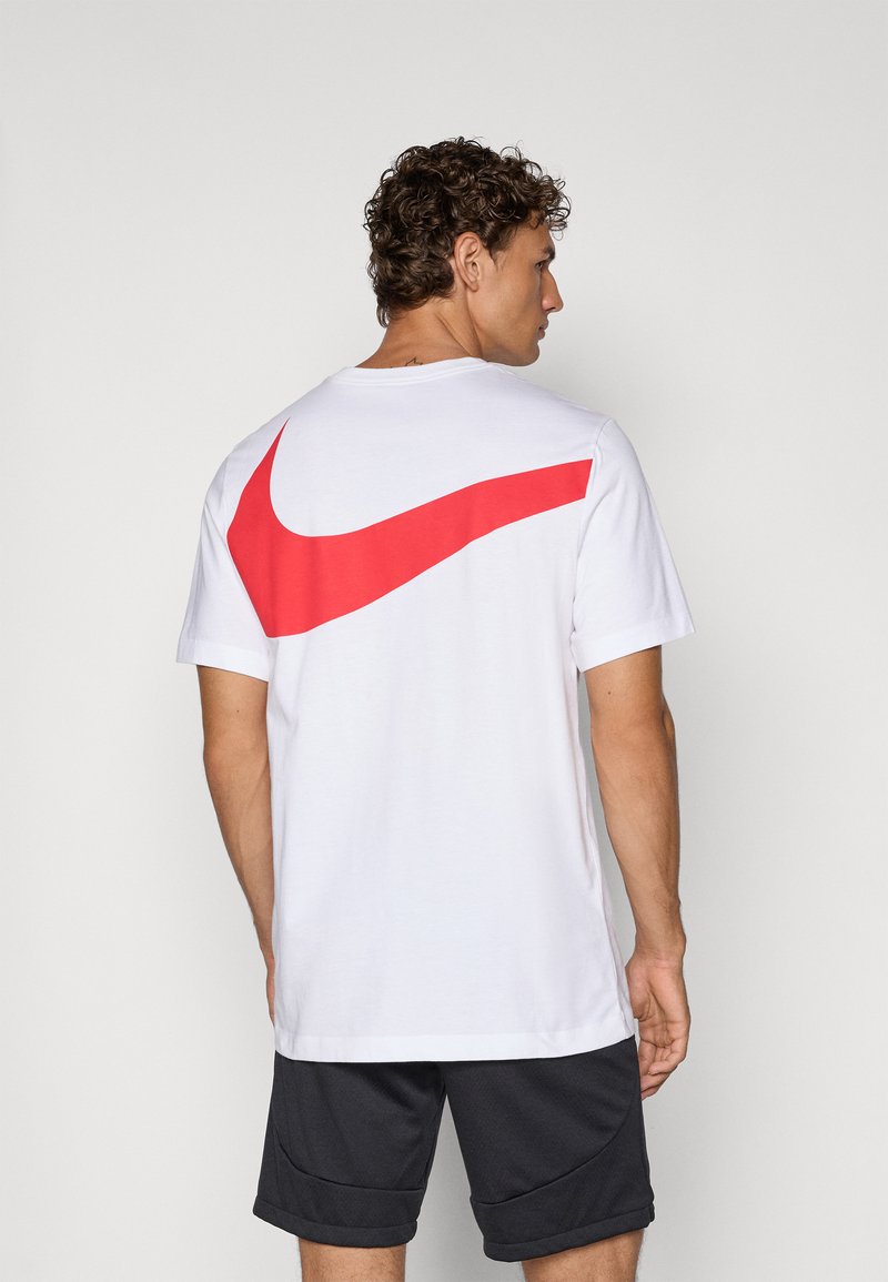Witte t-shirt met korte mouwen, voorzien van een groot rood Nike swoosh-logo op de achterkant. De stof lijkt soepel te zijn, met een relaxte pasvorm.