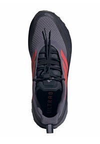 Chaussure de sport grise et noire avec des accents rouges, empeigne texturée, bout rond, système de laçage à l'avant et tirant au talon.