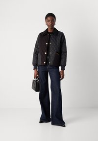 Quilted black jacket with a collar, gold buttons, and contrasting textured panels, paired with flared denim jeans and a small black handbag.