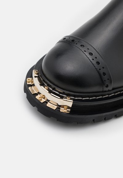 Schwarze Lederstiefelette mit runder Zehenform, goldfarbenen Hardware- Akzenten und detaillierter Naht. Sie verfügt über eine robuste schwarze Sohle für besseren Halt.