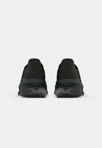 Paire de chaussures de sport noires vues de dos avec un talon texturé et une semelle épaisse sur un fond clair uni.