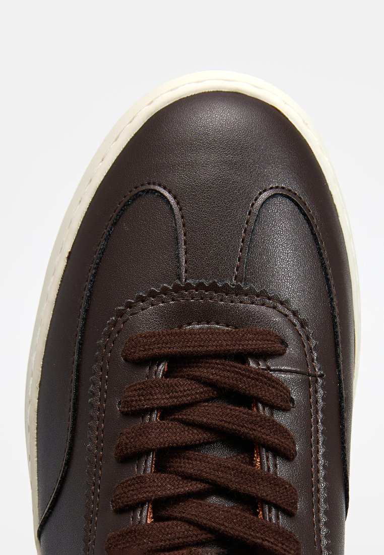 Brązowe skórzane trampki z zaokrąglonym noskiem, grubą białą podeszwą, brązowymi sznurowadłami i przeszyciami w gładkiej fakturze.