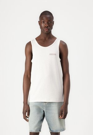 Kergehall tank top ümmarguse kaelusega, millel on rindkere kohal väike punase ja musta horisontaalne logo graafika. Kanti siniste denim lühikesed püksid.