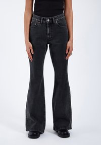 High-waisted black flared jeans made of denim, featuring front pockets, copper rivets, and a contrast stitched hem. Smooth texture.