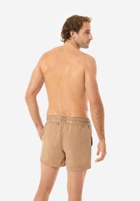 Pantaloni da bagno marroni con vita elasticizzata, caratterizzati da una texture liscia e una lunghezza corta, mostrati su un modello maschile visto da dietro.