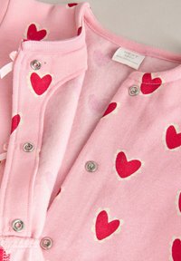 Rosa babykofta med röda hjärtmönster, tryckknappar och mjukt innerfoder. Har ribbad halsringning och fåll. Material av bomullsblandning.