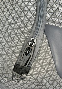 Tessuto grigio con trama e motivo geometrico, caratterizzato da una cerniera argento e componenti nere. Dettaglio in pelle liscia vicino alla cerniera.