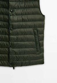 Veste matelassée sans manches vert foncé avec boutons-pression et poche latérale verticale sur fond blanc.
