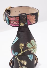 Sandale à talons en satin noir ornée de broderies florales vives en rose, bleu et or, avec une bride à boucle au niveau de la cheville et un design à bout ouvert.