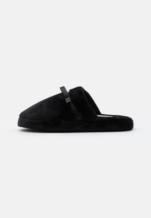 Sorte slippers lavet af blødt stof med en flad sål, prydet med en sløjfedetail på siden og et rundt tådesign.
