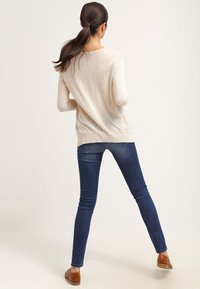 Pull beige clair à manches longues, coupe décontractée, ourlet côtelé, associé à un jean slim bleu foncé et des chaussures plates marron.