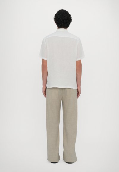 Camisa branca de manga curta feita de linho, combinada com calças largas em bege claro com um padrão texturizado. Vista traseira com bainha reta.