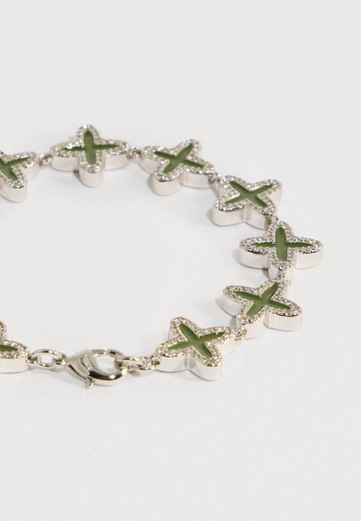 Pulseira de prata com incrustações verdes em forma de cruz, ligadas por pequenas correntes, com fecho de lagosta, sobre um fundo branco.