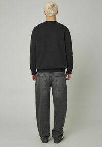 Sweat-shirt noir à col rond et poignets côtelés, associé à un jean gris délavé, ample, avec des poches arrière.