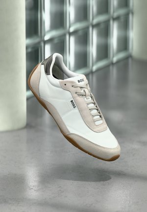 Valge ja beež BOSS toss pruunide talladega, hõljumas poleeritud betoonpõranda kohal klaasplokkseinaga taustal.