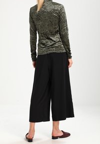 Olivegrünes, strukturiertes Langarmoberteil, kombiniert mit locker sitzenden schwarzen Culottes; verfügt über einen glatten Stoff und minimale Hardware-Akzente.