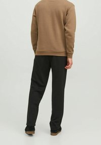 Sudadera marrón de manga larga, con puños y dobladillo acanalados. Combinada con pantalones negros, de corte recto y textura suave.