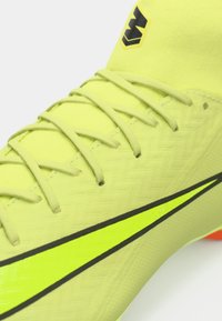 Spilgti dzelteni futbola zābaki ar teksturētu virsmu, melniem akcentiem un atstarojošiem elementiem uz zīmola. Iekļauti gaiši pelēki šņores.