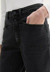 Vaqueros de mezclilla negra con cintura alta, que cuentan con cierre de doble botón, bolsillo delantero y una textura ligeramente desgastada.
