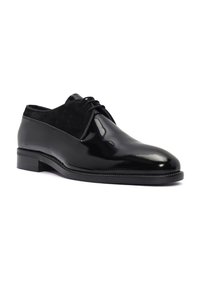 Chaussure en cuir noir avec une finition brillante, dotée d'un dessus en daim, d'un bout arrondi et d'un design à lacets. Talon bas empilé et couture minimaliste.