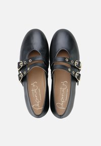 Zapatos de cuero negro con punta redondeada y dos correas ajustables con hebillas en tono dorado. Textura suave con una plantilla marrón.