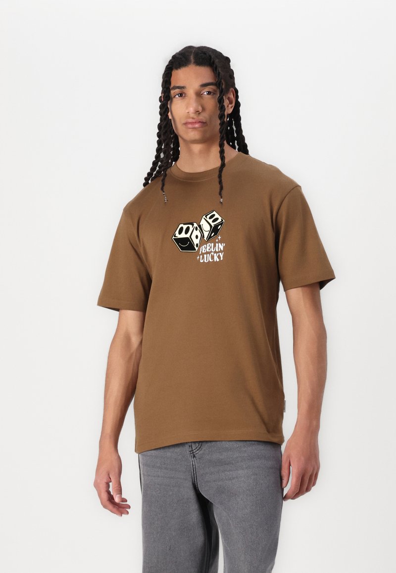 Brun bomulds t-shirt med grafisk print af to terninger og teksten "Feelin' Lucky" i creme og sort. Korte ærmer og afslappet pasform.